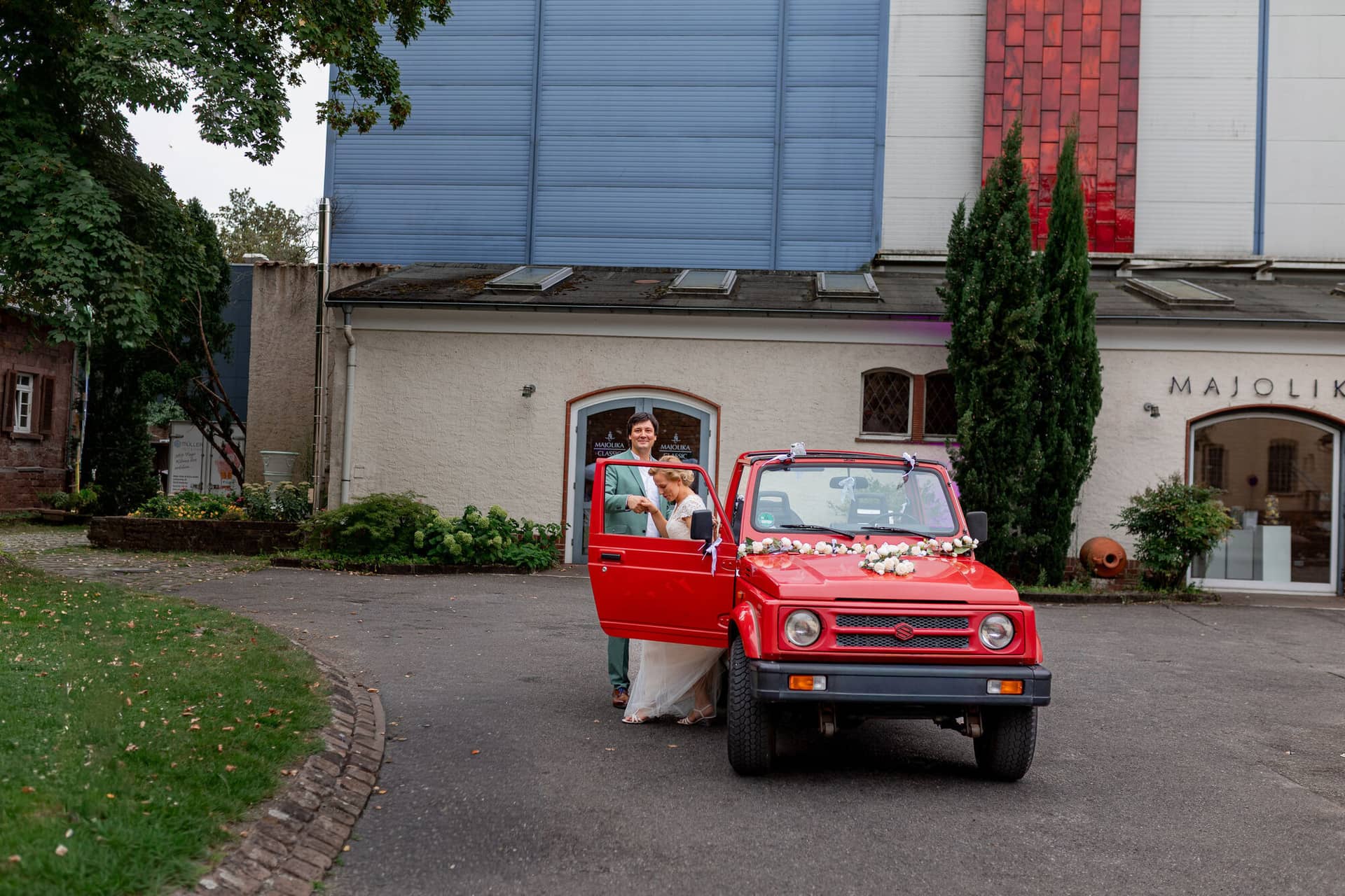 Hochzeitsfotograf Karlsruhe Daniela Matthias 20230819 15 20 27 4K8A6711.BvOmsc8v Rotes Fahrzeug mit Braut vor dem modernen Eingangsbereich der Hochzeitslocation in Karlsruhe
