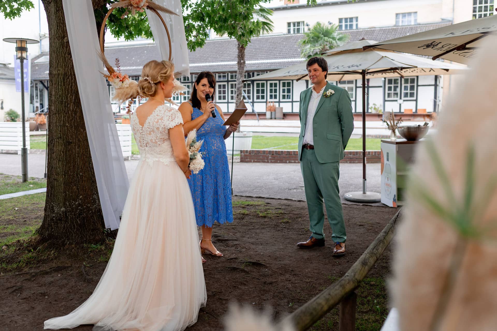 Hochzeitsfotograf Karlsruhe Daniela Matthias 20230819 15 24 56 4K8A7035.CtydQ2zH Braut hält eine Ansprache bei der freien Trauung, Bräutigam steht ihr gerührt gegenüber im Garten