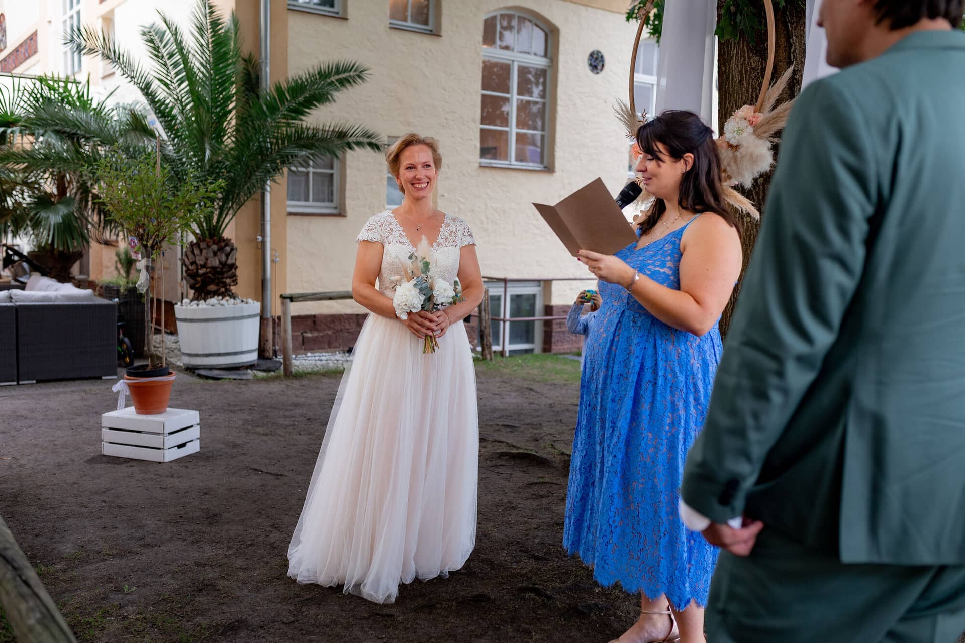 Hochzeitsfotograf Karlsruhe Daniela Matthias 20230819 15 28 20 4K8A7096.DQRtxfT5 Bräutigam liest seine Liebesworte vor, Braut steht ihm strahlend bei der Gartenhochzeit gegenüber