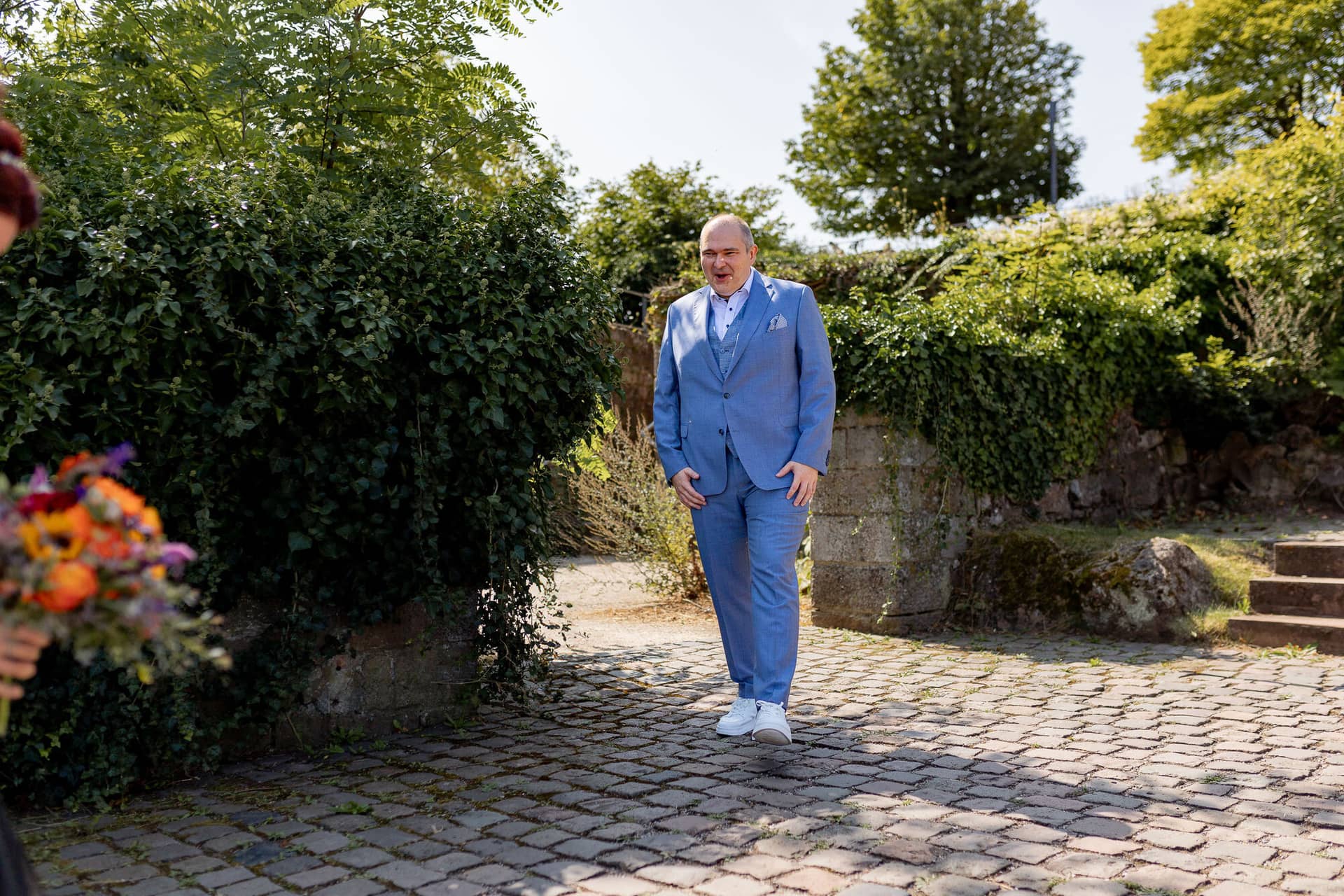 Hochzeitsfotograf Neustadt Hambacher Schloss Ruppertsberg Kellers Keller 09.DDw5pbBw Bräutigam in blauem Anzug wartet auf Braut beim First Look auf Kopfsteinpflaster vor historischer Mauer