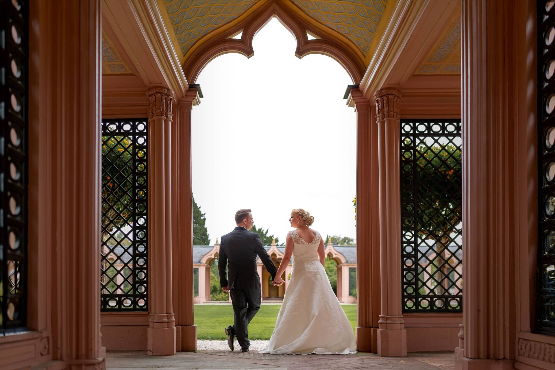 Hochzeitsfotograf Schwetzingen Schlossgarten Brautpaarshooting 20170812 14 30 32 IMG 0275.DuoaJpNs Brautpaar spaziert Hand in Hand durch das reich verzierte Portalbogentor im Schlossgarten Schwetzingen
