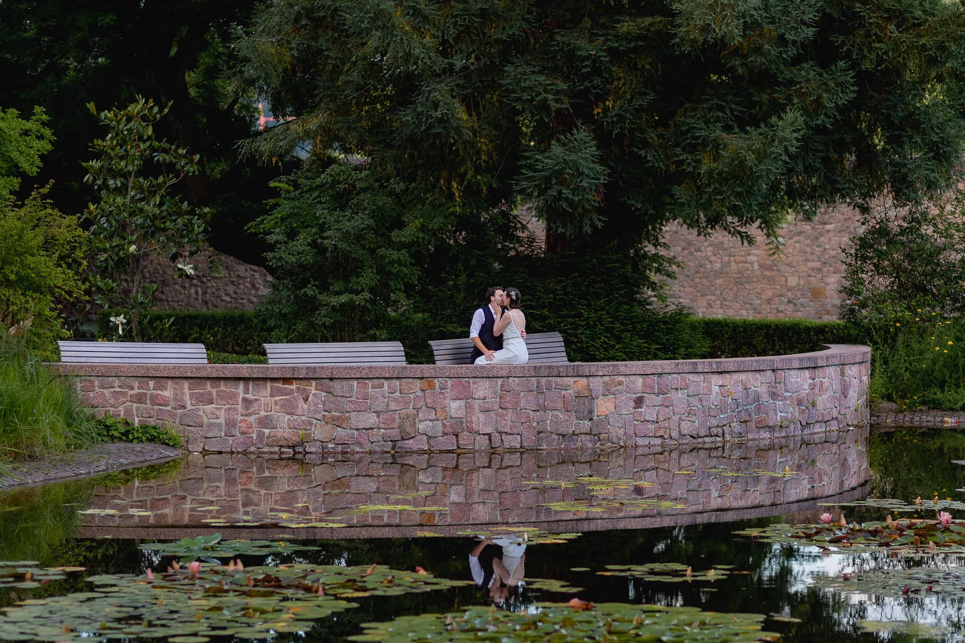 Julia Dennis Hochzeit Mannheim Brautpaarshooting Schlosspark Weinheim 4k8a0619.B7jfD PK Brautpaar sitzt auf einer Brücke im Schlosspark Weinheim und blickt über den Teich im Dunkeln