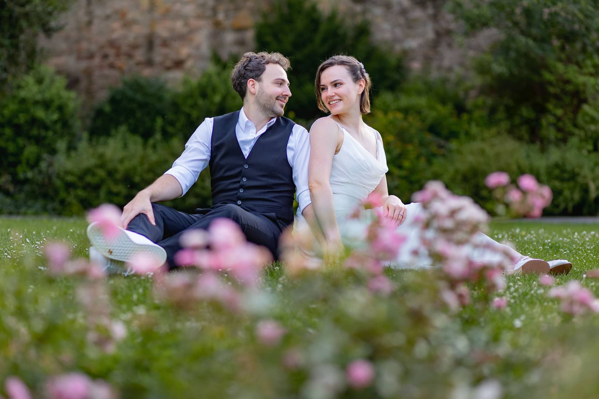 Julia Dennis Hochzeit Mannheim Brautpaarshooting Schlosspark Weinheim 4k8a0944.D6pfjQln Brautpaar sitzt zusammen umgeben von Blumen im Schlosspark Weinheim