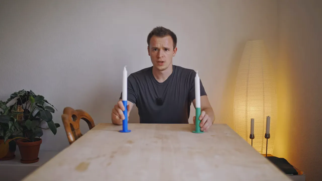 Moderator hinter Tisch mit zwei Kerzen in blauem und grünem Halter als Farbbeispiel