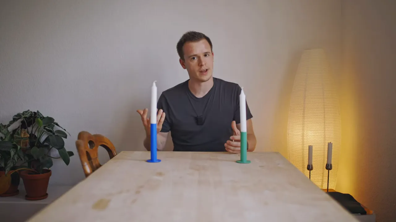 Person erklärt Primärfarbe; zwei Kerzenhalter in Blau und Grün auf einem Tisch, warme Lampe im Hintergrund.