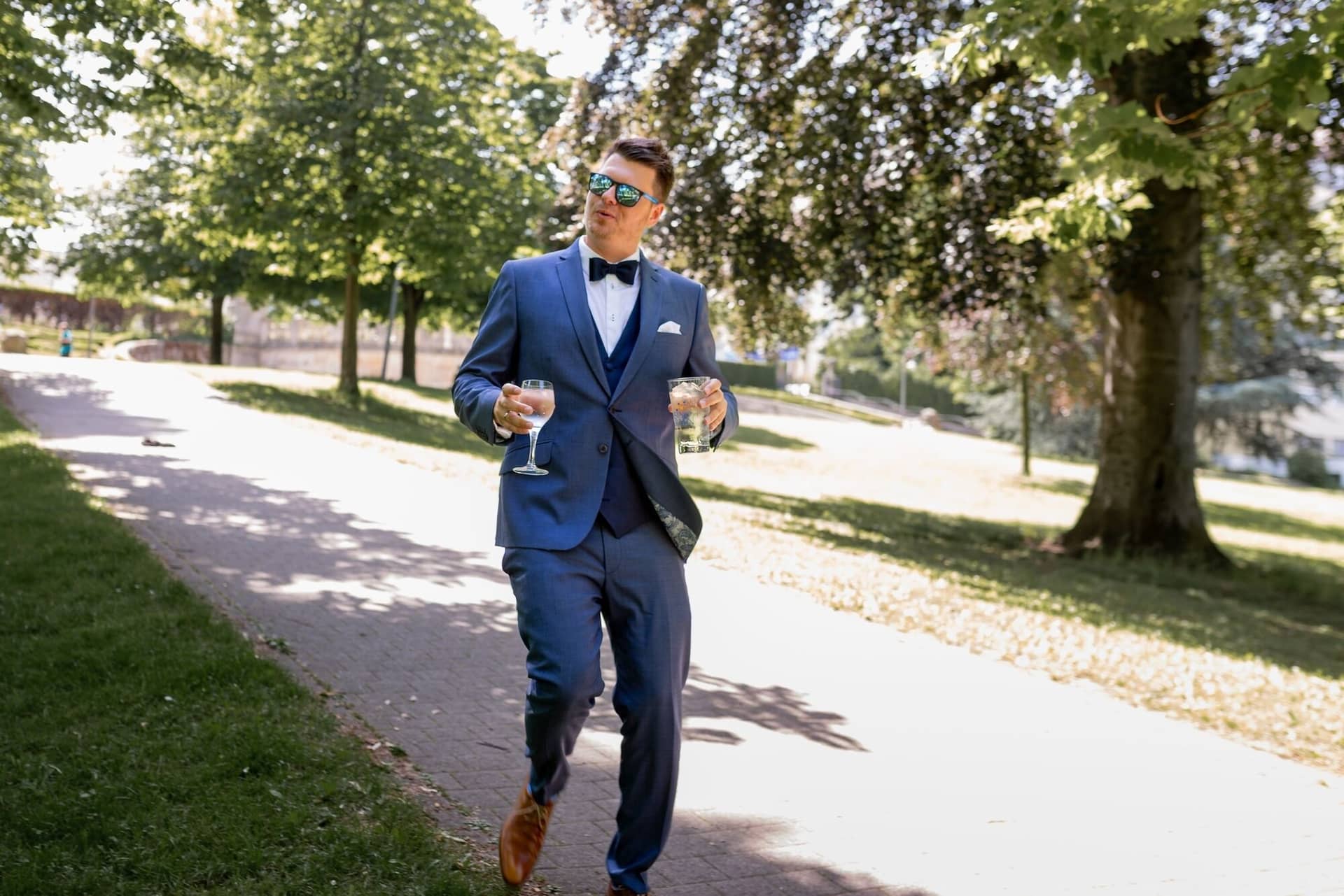Standesamtliche Trauung Mutterstadt Altes Rathaus Bad Duerkheim Schlossgarten IMG 3368.COYNmoez Bräutigam im blauen Anzug schlendert entspannt mit Prosecco-Glas entlang des Bachs im Kurpark Bad Dürkheim