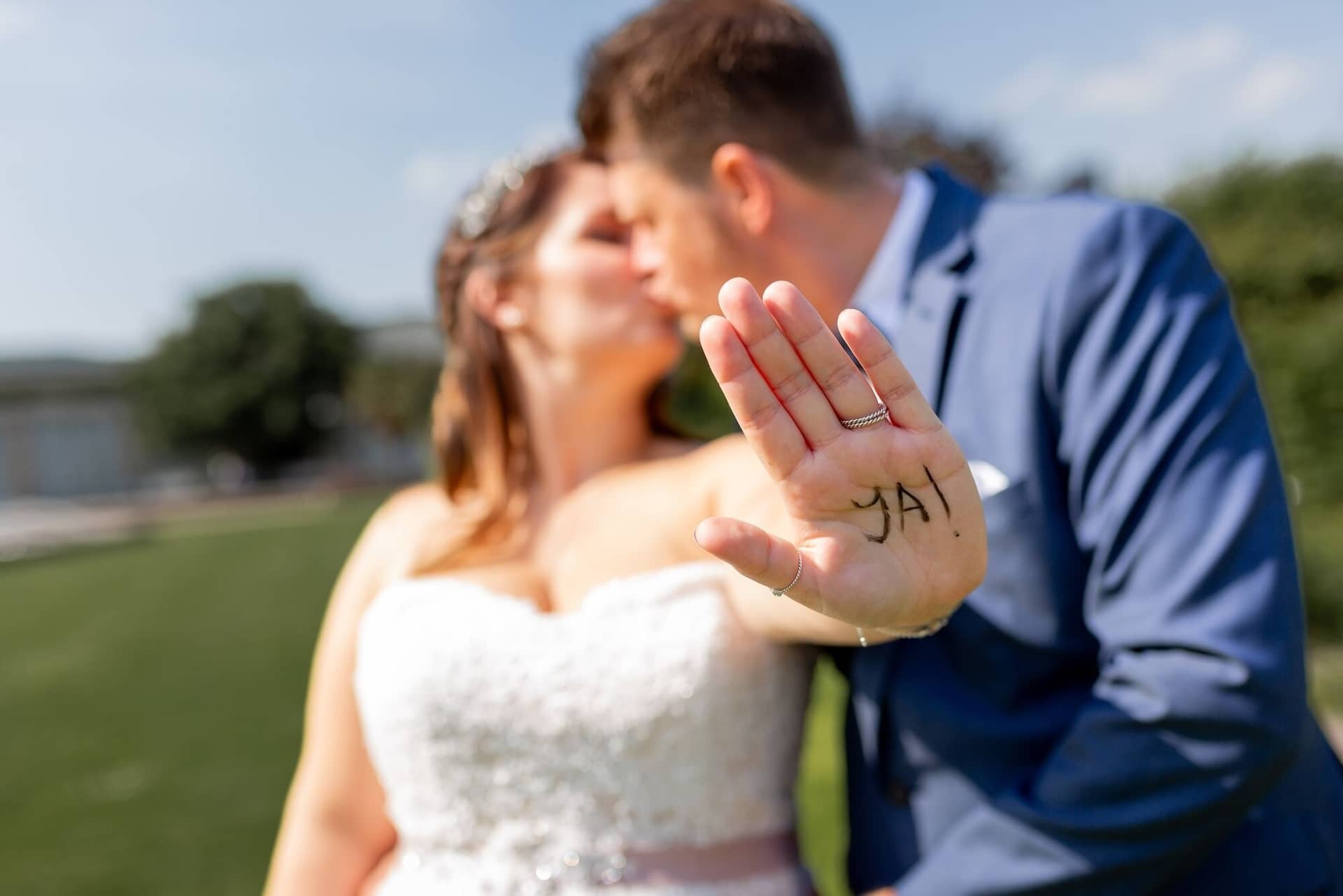 Standesamtliche Trauung Mutterstadt Altes Rathaus Bad Duerkheim Schlossgarten IMG 3878.LYLYO3FE Brautpaar küsst sich, Bräutigam zeigt Hand mit aufgeschriebenem "JA" im Kurpark Bad Dürkheim