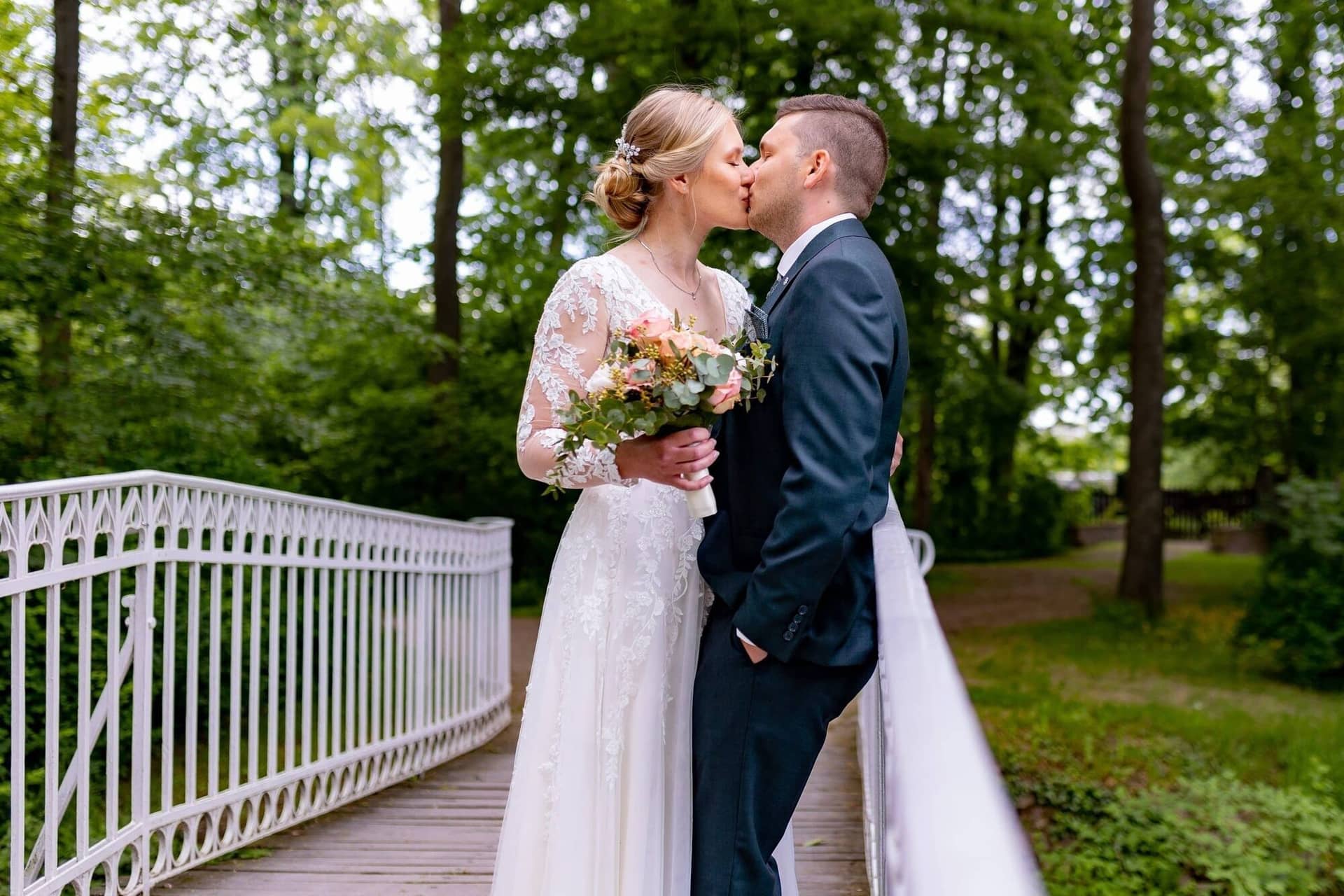 Verena Marius Hochzeitsfotograf Fotograf Worms Mettenheim 06.BIfq51BD Brautpaar küsst sich auf der kleinen Holzbrücke im Schlossgarten, umgeben von dichtem Grün