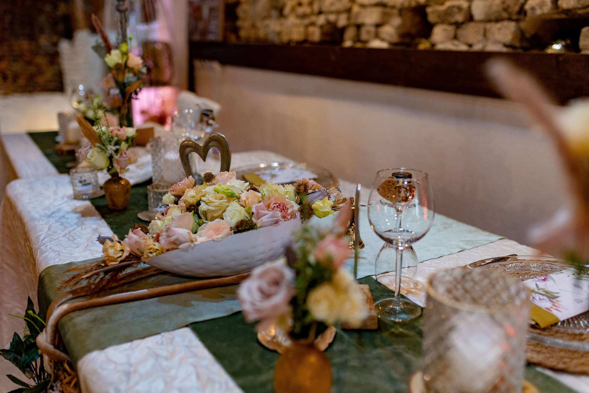Verena Marius Hochzeitsfotograf Fotograf Worms Mettenheim 13.Cey7hthC Langer Festtisch mit großer weißer Schale aus Pastellblüten und Kristallgläsern vor rustikaler Steinwand mit rosafarbener Beleuchtung