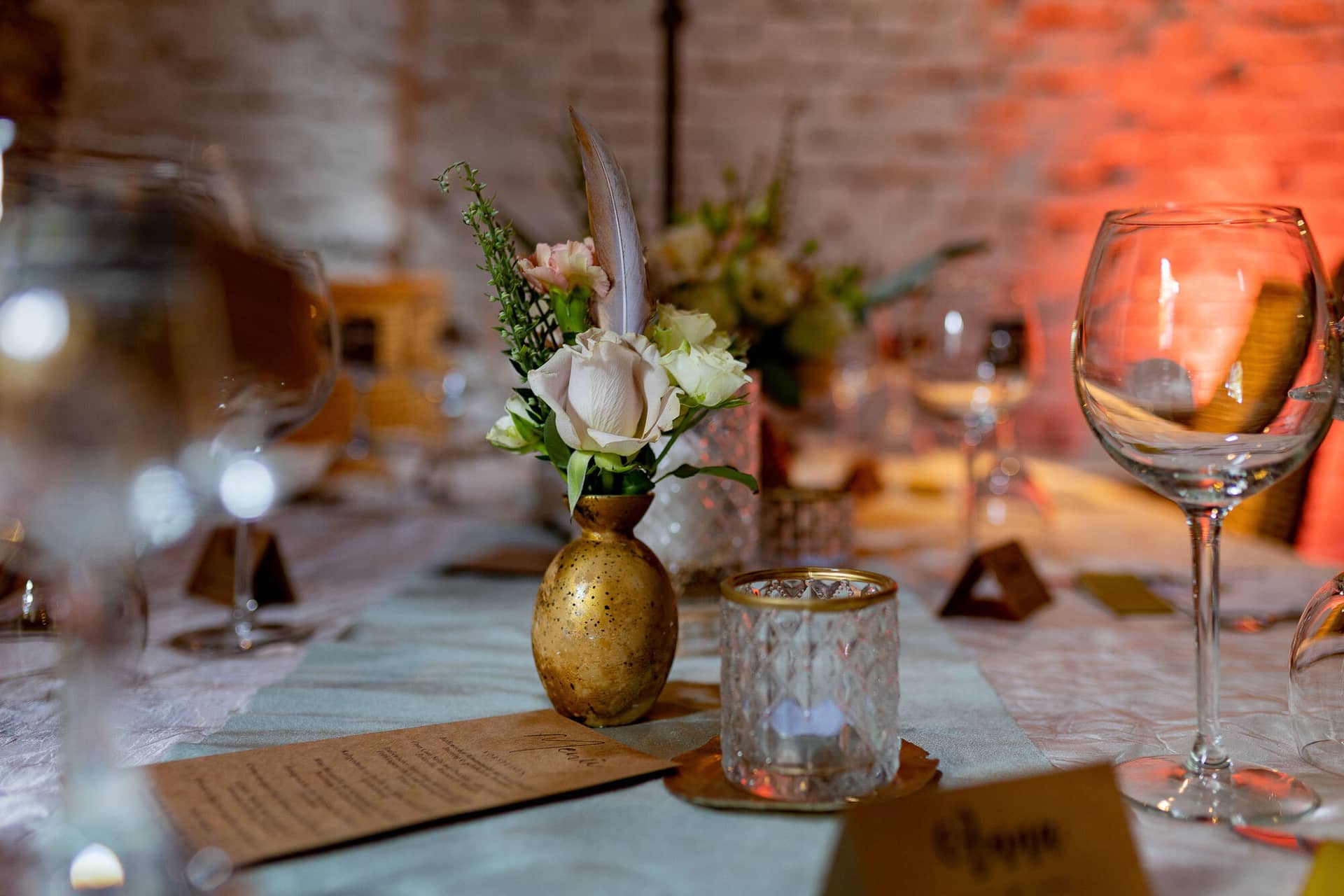Verena Marius Hochzeitsfotograf Fotograf Worms Mettenheim 15.THCUubG4 Tischdetail mit Menükarte, Blumenvase, Kerze und Weinglas vor der charakteristischen Backsteinwand