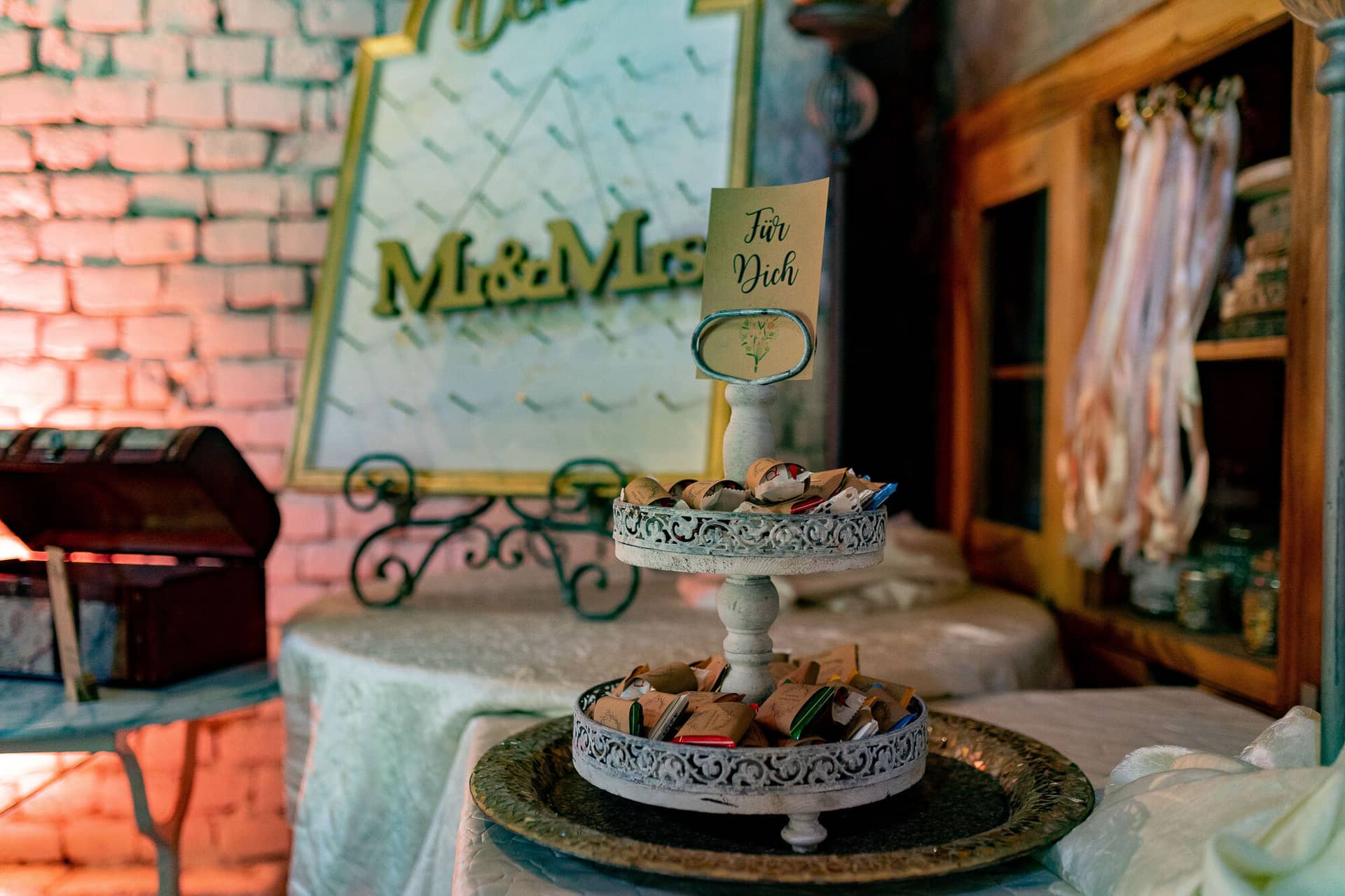 Verena Marius Hochzeitsfotograf Fotograf Worms Mettenheim 16.SNzL3b5k Tablett mit goldenen Glücksbringern als Gastgeschenke, Holzschild "Mr & Mrs" vor der Ziegelwand