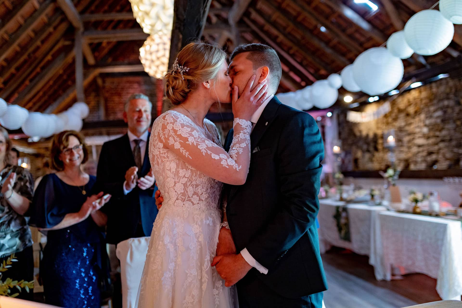 Verena Marius Hochzeitsfotograf Fotograf Worms Mettenheim 21.BmMxj8je Brautpaar küsst sich vor den jubelnden und klatschenden Gästen im rustikalen Festsaal des Dach der Welten