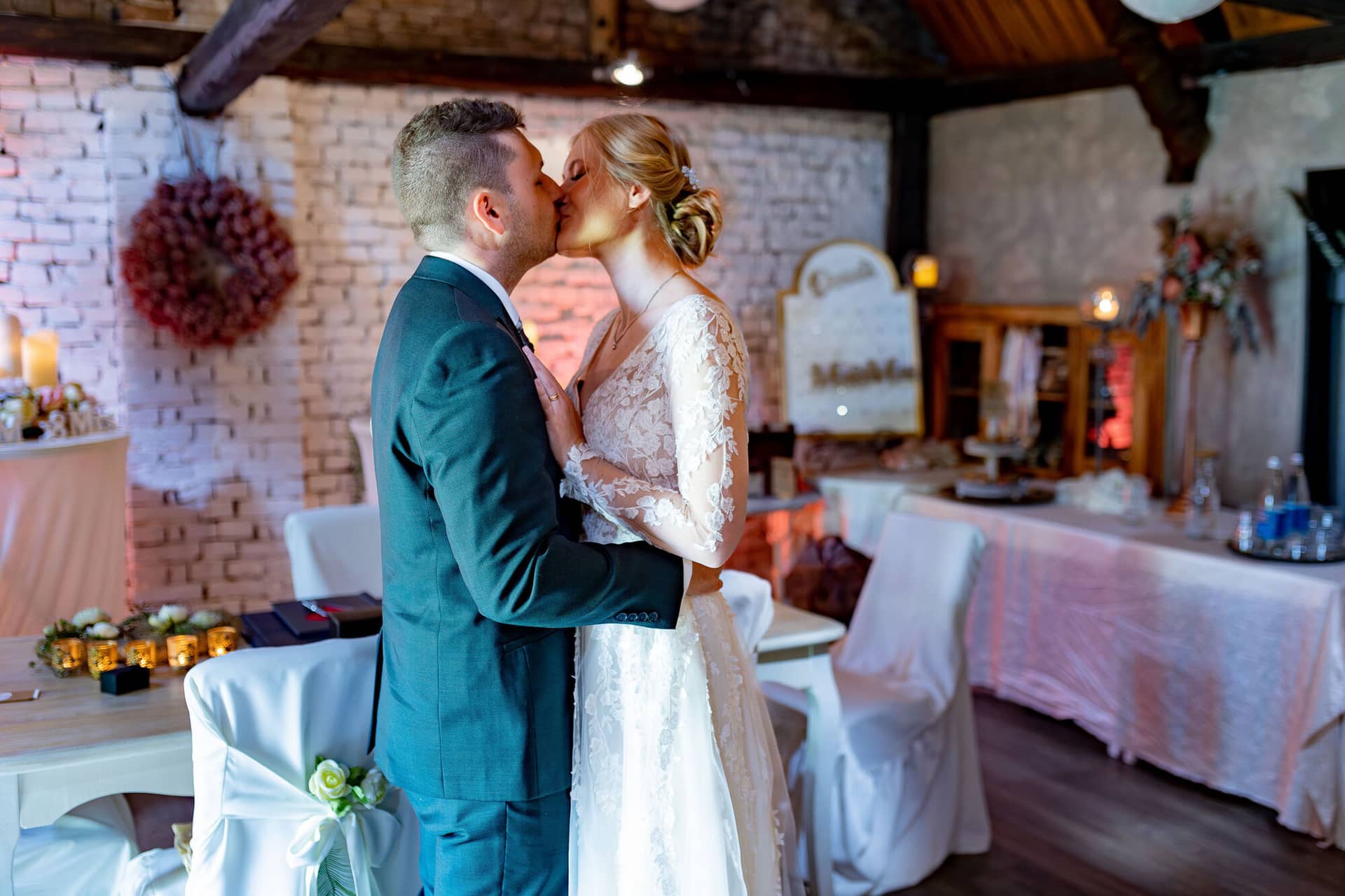 Verena Marius Hochzeitsfotograf Fotograf Worms Mettenheim 22.BaP1FfQA Brautpaar küsst sich innig im Steingemäuer-Innenraum mit Holzbalken und Lichtgirlanden